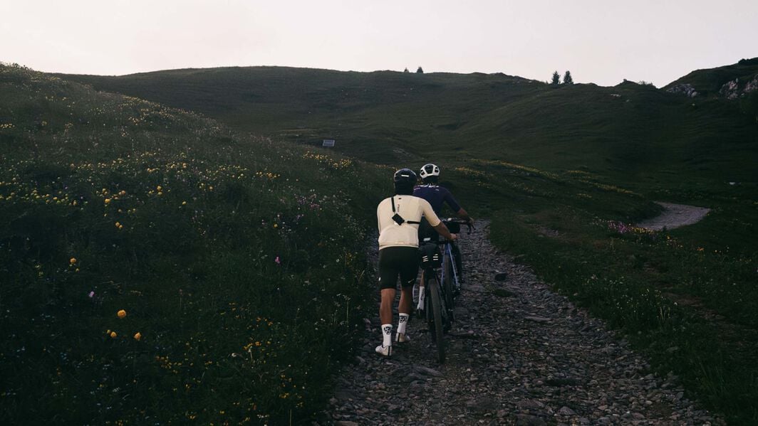 Un cycliste gravel avec des accessoires montés sur son vélo roule sur un sentier poussiéreux, affichant plusieurs équipements pour les aventures tout-terrain